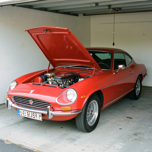 Coupé sportif britannique classique rouge présenté dans un garage, capot ouvert et détails mécaniques visibles.